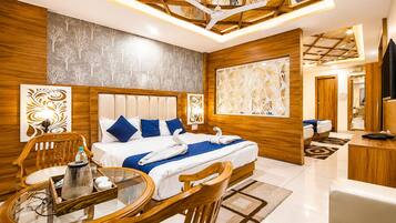 A hotel room with a large bed, a sitting area with a table and chairs, a TV, and a decorative wall panel.