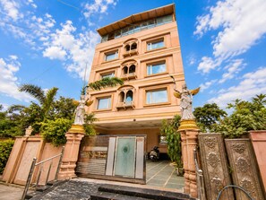 Un edificio de varios pisos con una entrada destacada, una estatua y un camino de acceso con portones.