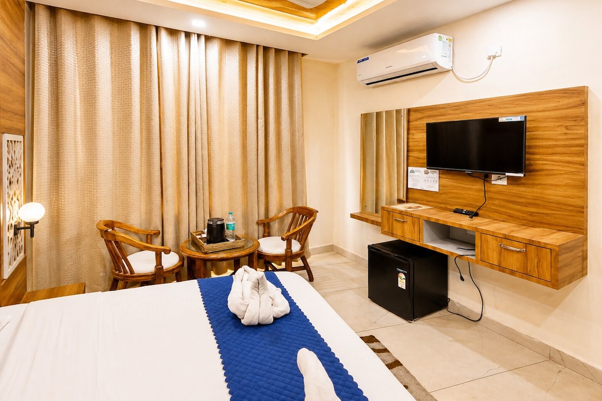 A hotel room with a bed, a desk, a television, and an air conditioning unit.