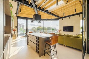 A modern kitchen with a large island, wooden ceiling beams, and a view of the city. - The Penthouse Fulham/West Kensington 3 Bedrooms (London)