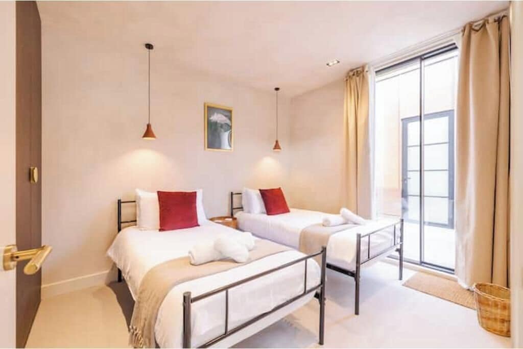 A hotel room with two beds, a window with curtains, and a painting on the wall.
