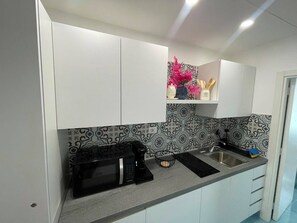 A kitchen with white cabinets, a black microwave, a sink, and patterned backsplash. - Sweet Home Luna: a charming apartment in the heart of Amalfi (Amalfi)