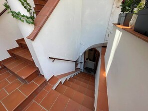 Uma escadaria com ladrilhos de barro avermelhado e uma parede branca, que leva a um andar superior.