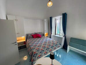 A bedroom with a bed, bedside table, lamp, window with curtains, and a bench. - Sweet Home Luna: a charming apartment in the heart of Amalfi (Amalfi)