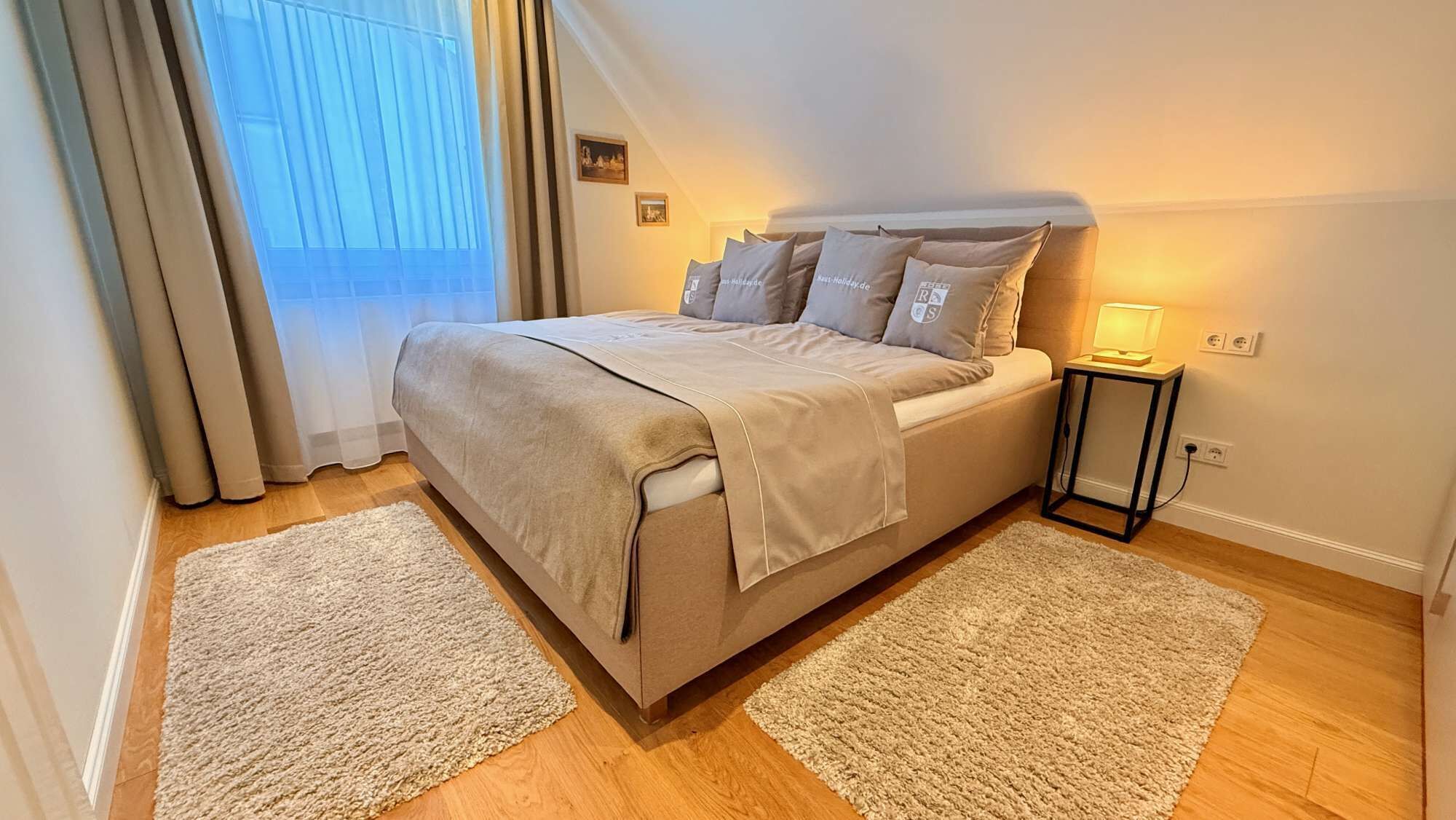 Ein Schlafzimmer mit einem Bett, zwei Nachttischen, einem Fenster mit Vorhängen und einem Wandbild.