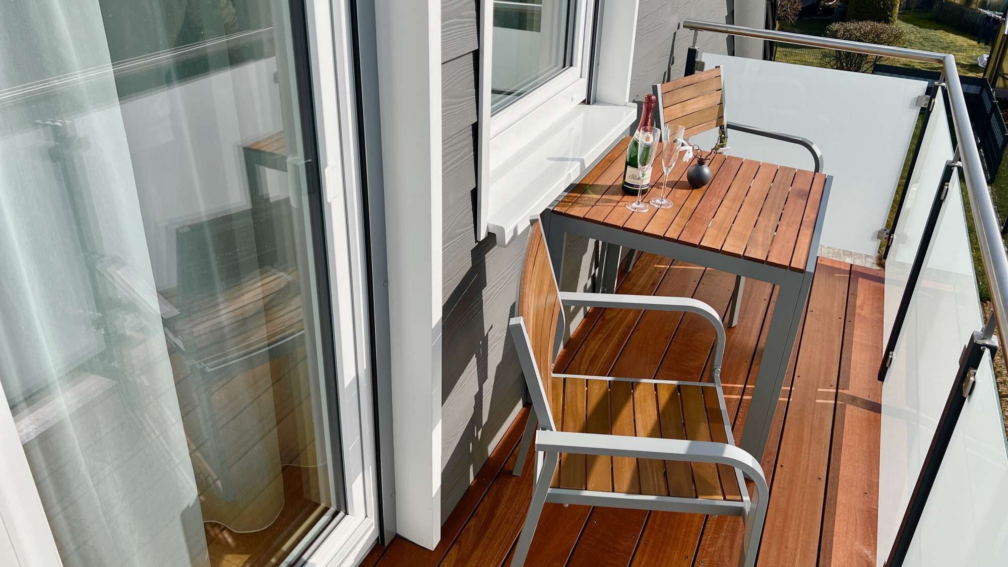 Ein Balkon mit Holztisch, zwei Stühlen und einer Champagnerflasche.