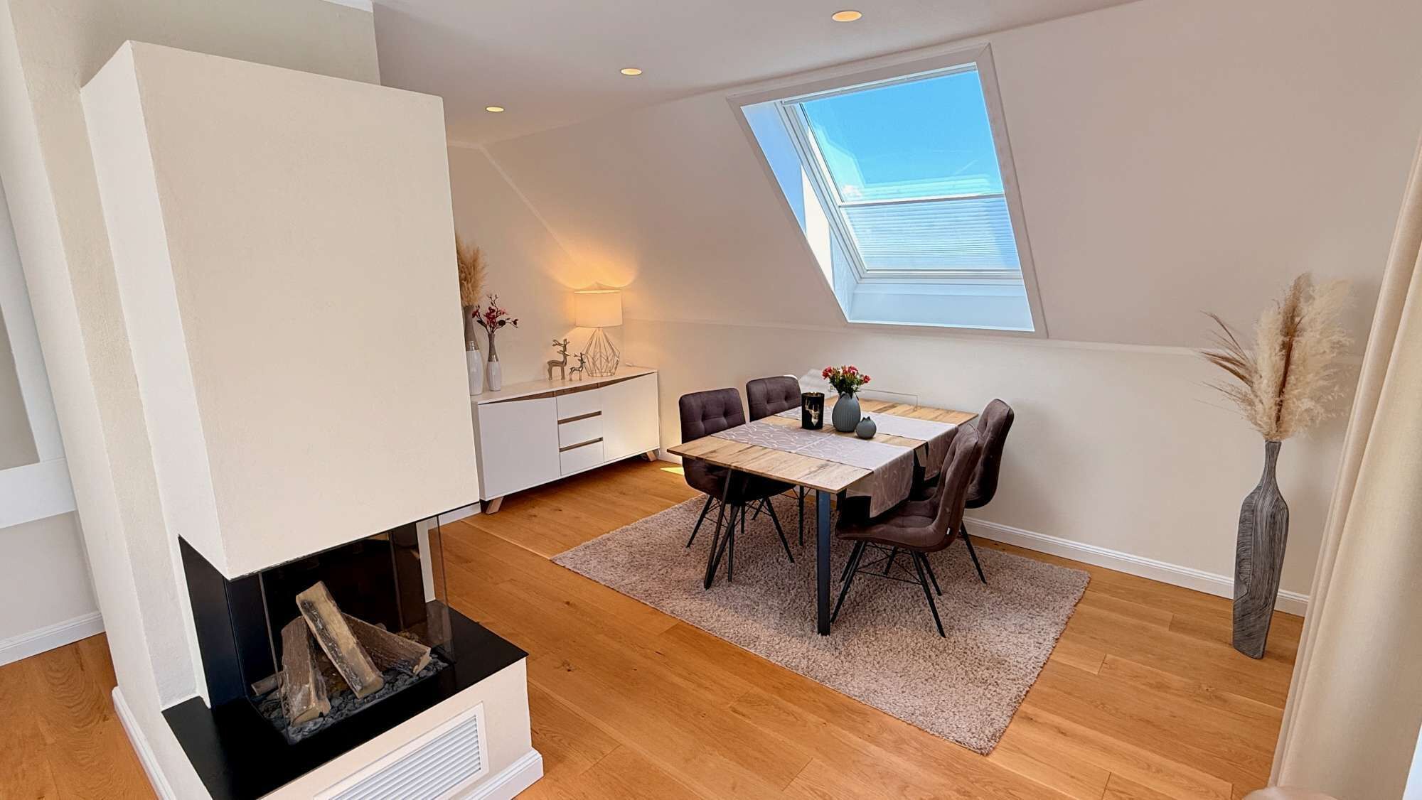 A modern living room with a dining area, a fireplace, and a skylight.