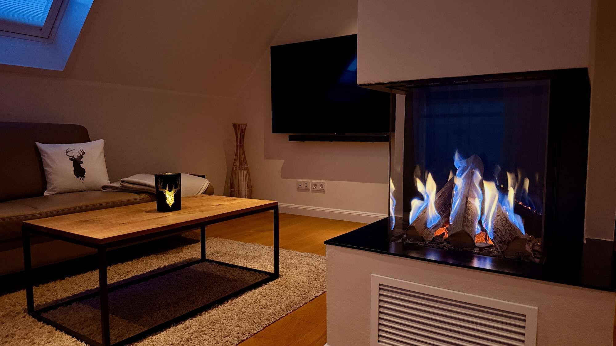A modern living room with a fireplace, a sofa, a coffee table, and a flat-screen TV mounted on the wall.