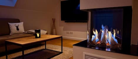 A modern living room with a fireplace, a sofa, a coffee table, and a flat-screen TV mounted on the wall.