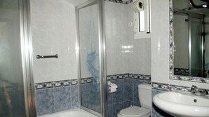 A bathroom with a glass-enclosed shower, a toilet, and a sink. - Apartamento Caracola (Chipiona)