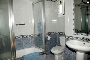 A bathroom with a glass-enclosed shower, a toilet, and a sink. - Apartamento Caracola (Chipiona)