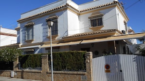A two-story building with a tiled roof, a gated entrance, and a well-maintained hedge. - Apartamento Caracola (Chipiona)