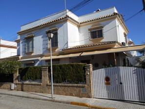 A two-story building with a tiled roof, a gated entrance, and a well-maintained hedge. - Apartamento Caracola (Chipiona)