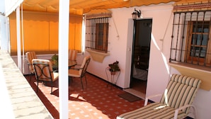 A covered outdoor seating area with chairs and a table, a door leading to an interior space, and a window with bars. - Apartamento Caracola (Chipiona)