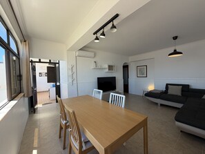 A modern living room with a wooden dining table, white chairs, a black sofa, and a TV. - Gale Beach Walk T3 Apartment (Albufeira)
