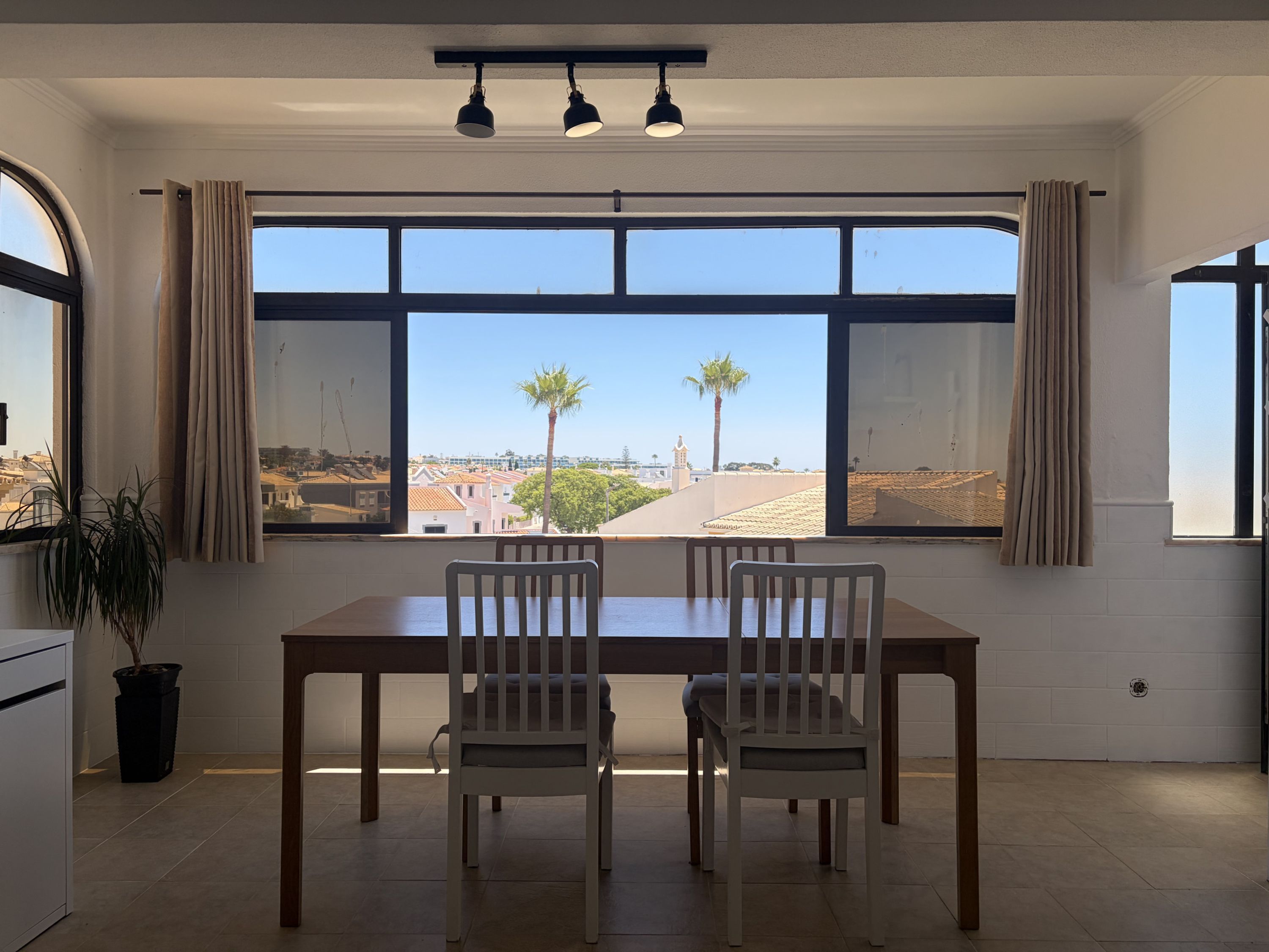 A dining area with a large window, two chairs, a table, and a potted plant.