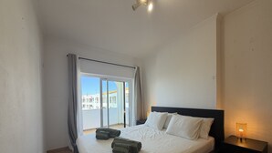 Habitación de hotel con cama, mesita de noche, lámpara y vista a edificios a través de una ventana.