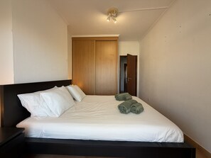 Ein Hotelzimmer mit einem Bett, einem Nachttisch, einem Holzschrank und einer Tür zu einem anderen Raum.