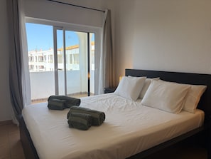 Ein Hotelzimmer mit einem Bett, zwei Kissen, einem Fenster mit Vorhängen und Blick auf Gebäude.