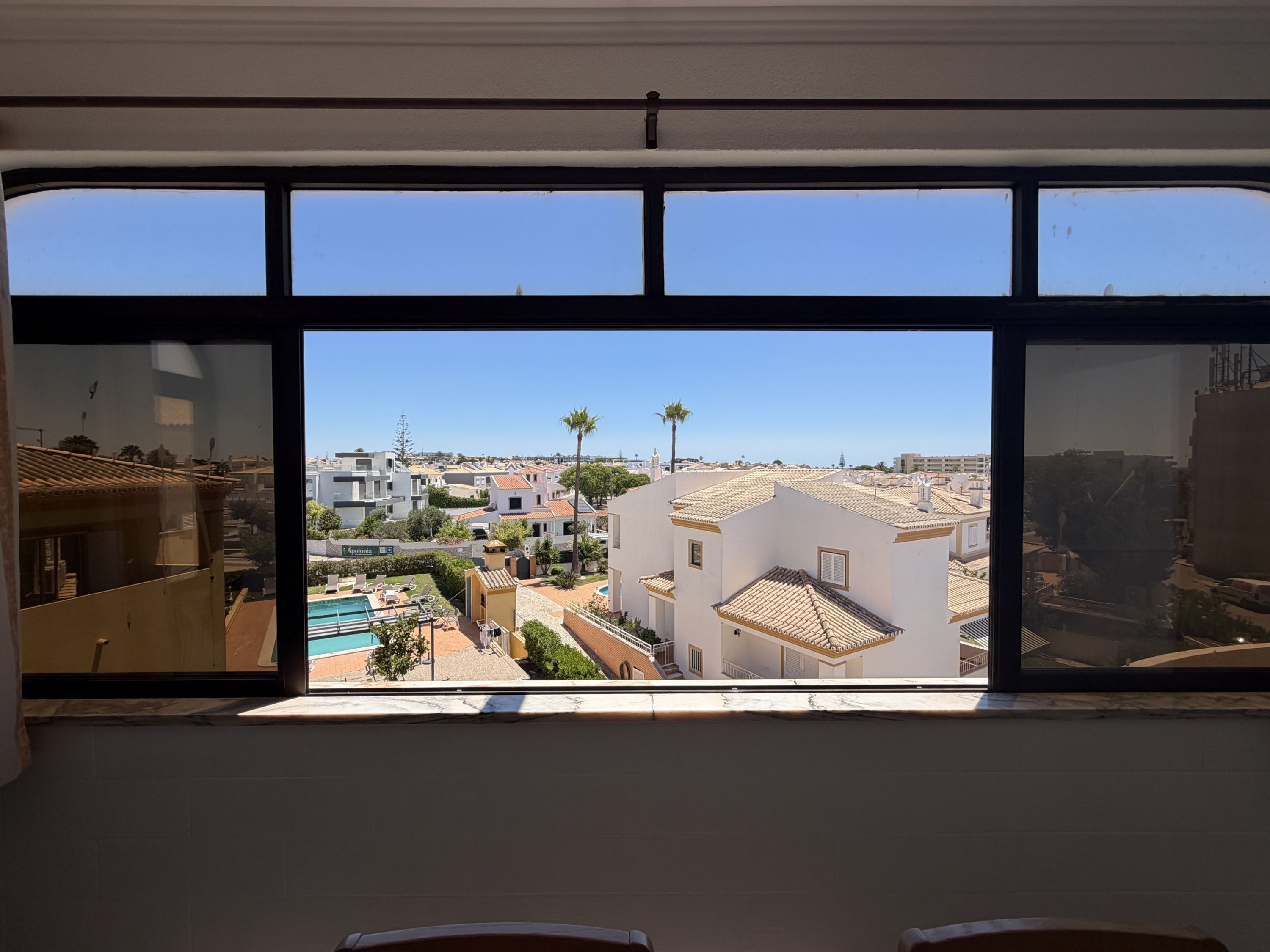 A view from a window with a clear sky, a pool, and buildings in the distance.