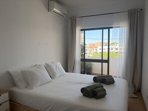 A hotel room with a bed, a window with curtains, and a view of buildings outside. - Gale Beach Walk T3 Apartment (Albufeira)