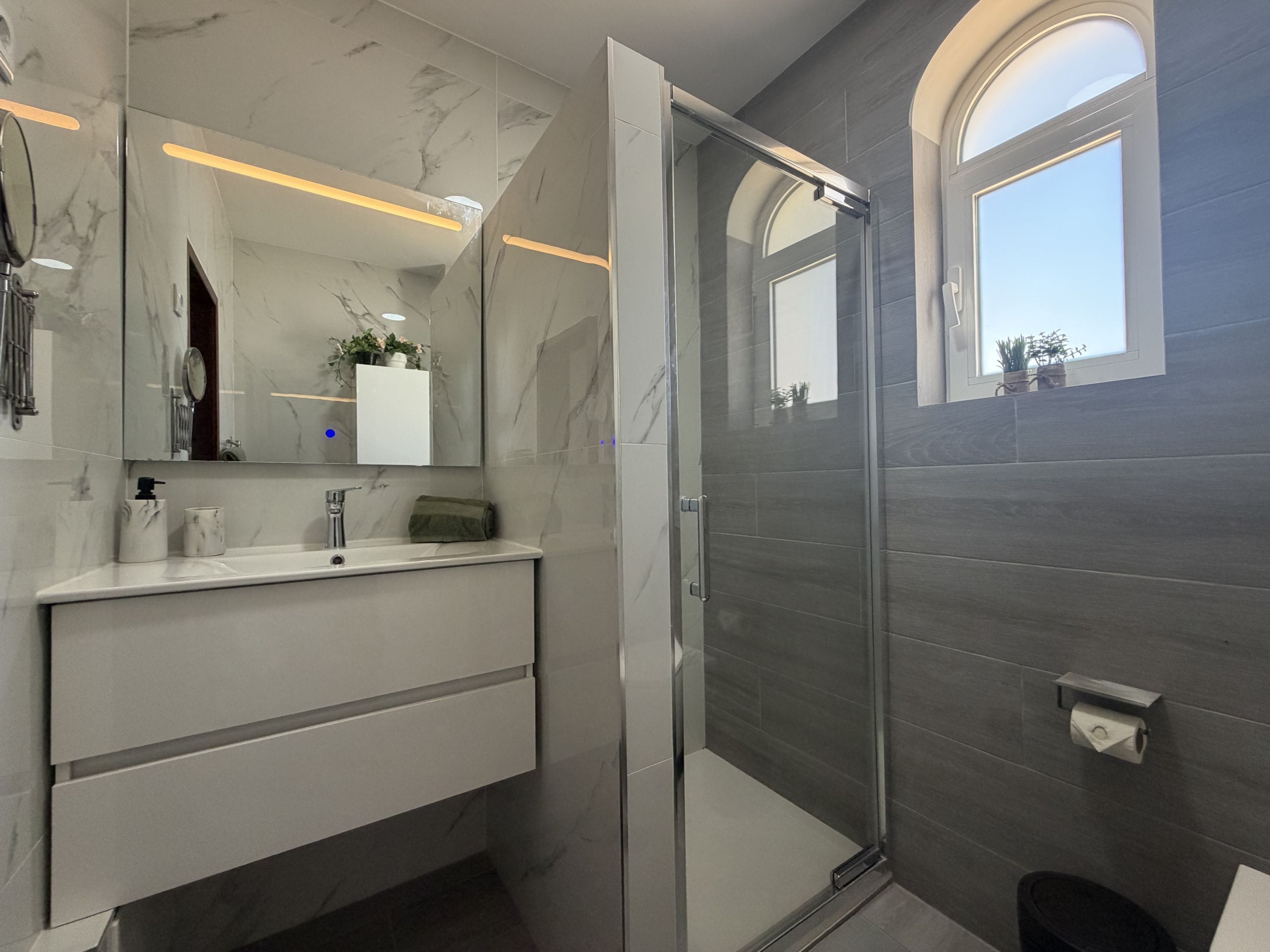 A modern bathroom with a glass shower enclosure, a marble vanity, and a large mirror.