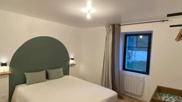 A bedroom with a bed, a window, a radiator, and a bedside table.