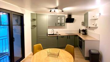 Een moderne keuken met een eetgedeelte, met een ronde tafel met stoelen, een zwarte prullenbak en een raam met uitzicht.