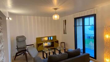 Een moderne woonkamer met een bank, een fauteuil, een salontafel en een tv-meubel. Er is een groot raam met uitzicht op het omliggende landschap.