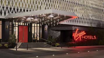 A hotel entrance with a modern design, featuring a prominent neon sign and a geometric facade.