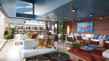 A spacious lobby with a modern design, featuring a seating area with sofas and chairs, a coffee table, and a large window offering a view of the outdoors.