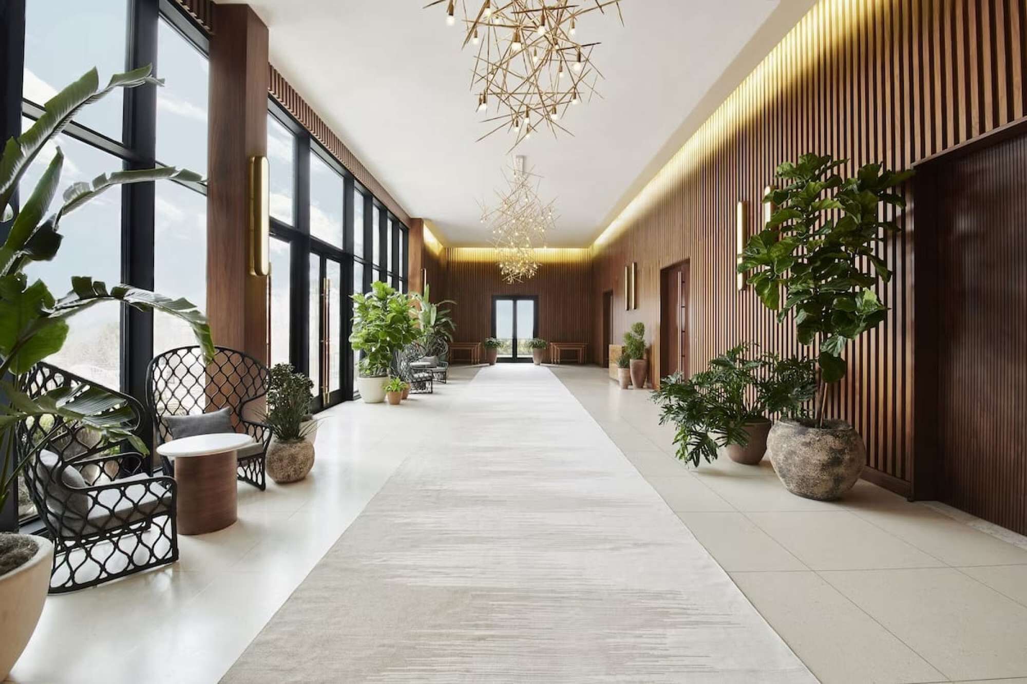 A spacious hallway with a central walkway, flanked by wooden paneling and potted plants.