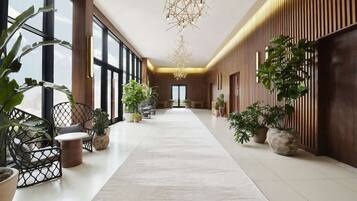 A spacious hallway with a central walkway, flanked by wooden paneling and potted plants.