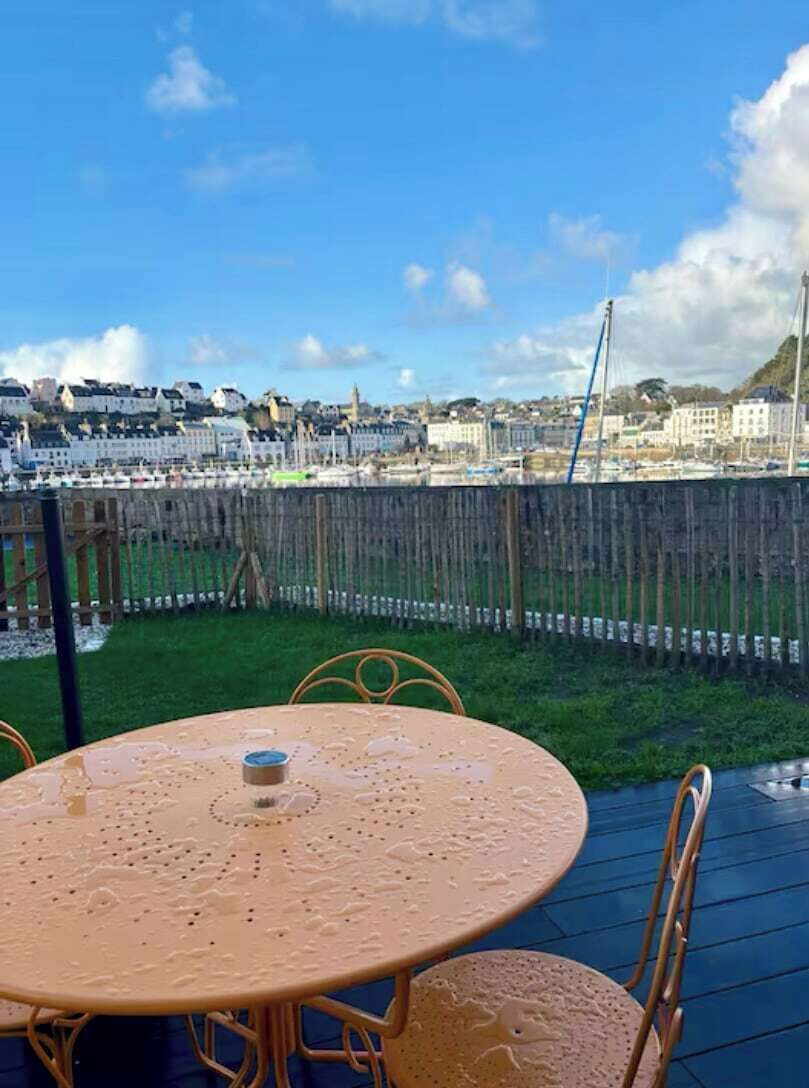 Une table ronde entourée de chaises, une clôture en bois et, en arrière-plan, une vue sur des bâtiments.