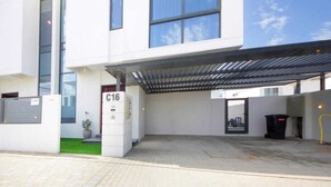 A modern building with a covered entrance, a number sign 'C16', and a small green area with a potted plant. - Modern Home w/ Rooftop Terrace in Prime Location (Al Hamriyah)