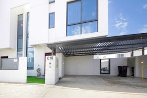 A modern building with a covered entrance, a number sign 'C16', and a small green area with a potted plant. - Modern Home w/ Rooftop Terrace in Prime Location (Al Hamriyah)