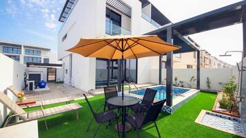 A modern outdoor patio with a pool, seating area, and a covered section.