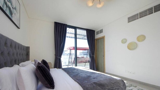 A bedroom with a bed, a window with curtains, a door, and wall decor. - Modern Home w/ Rooftop Terrace in Prime Location (Al Hamriyah)
