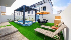 A modern outdoor patio with a pool, seating area, and a covered structure. - Modern Home w/ Rooftop Terrace in Prime Location (Al Hamriyah)