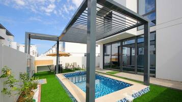 Ein moderner Poolbereich im Freien mit Glasverkleidung, Kunstgrasanlage und einer Pergola.