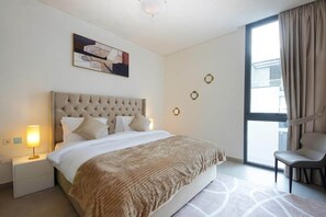 A hotel room with a large bed, a bedside lamp, a chair, and a window with curtains.