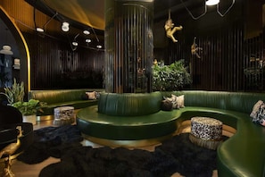 A modern lounge area with green curved seating, a central column, and decorative lighting. - Dallas' Design District Stay + Rooftop Pool & Bar (Dallas)
