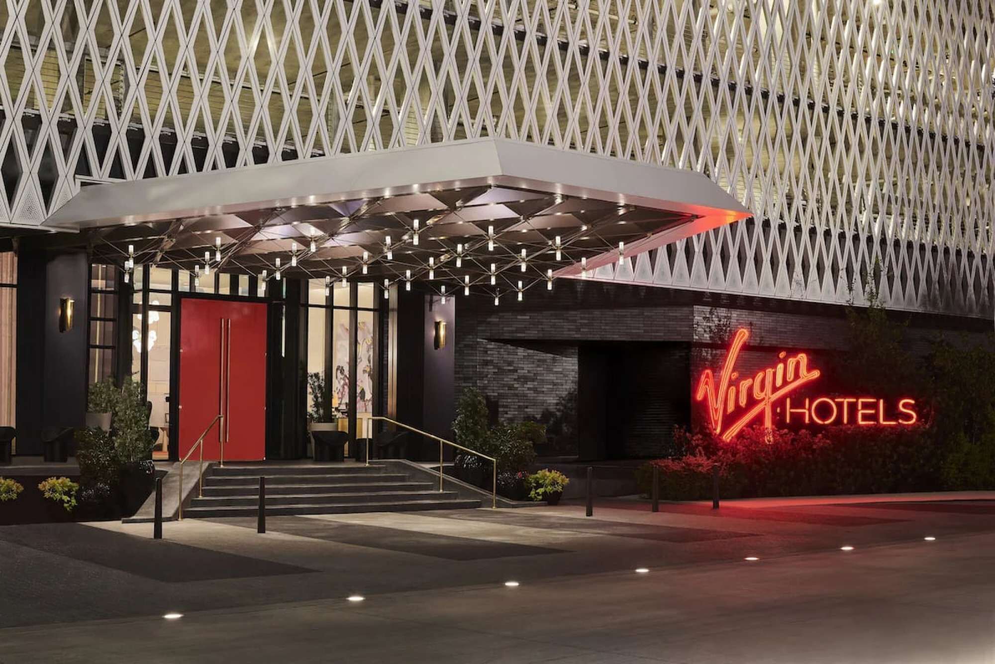 A hotel entrance with a modern design, featuring a prominent neon sign and a geometric facade.