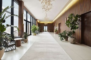 A spacious hallway with a central walkway, flanked by wooden paneling and potted plants. - Dallas' Design District Views + Rooftop Pool & Bar (Dallas)