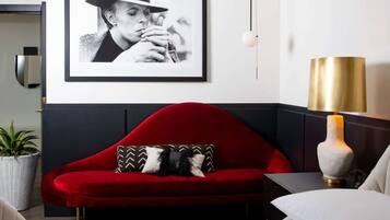 A red sofa with patterned pillows, a framed black and white photograph on the wall, and a gold lamp on a bedside table.