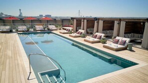 A rooftop pool with lounge chairs and umbrellas, a clear view of the city skyline, and a wooden deck. - Dallas' Design District Views + Rooftop Pool & Bar (Dallas)