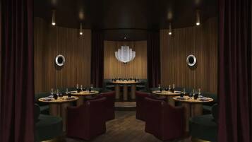 A room with a central round table, four chairs, a chandelier, and curtains.