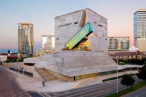 A modern building with a unique angular design, featuring a prominent glass facade and a sloped roof. - Dallas Skyline Views + Rooftop Pool. Bar. Fitness. (Dallas)