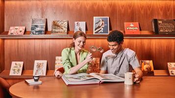 A wooden interior with a table displaying books and a coffee mug, and a shelf with various framed items.