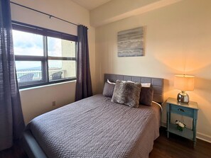 A bedroom with a bed, a nightstand, a lamp, a window with curtains, and a painting on the wall. - 6th floor condo- hot tub- views of Grandfather Mountain (Sugar Mountain)
